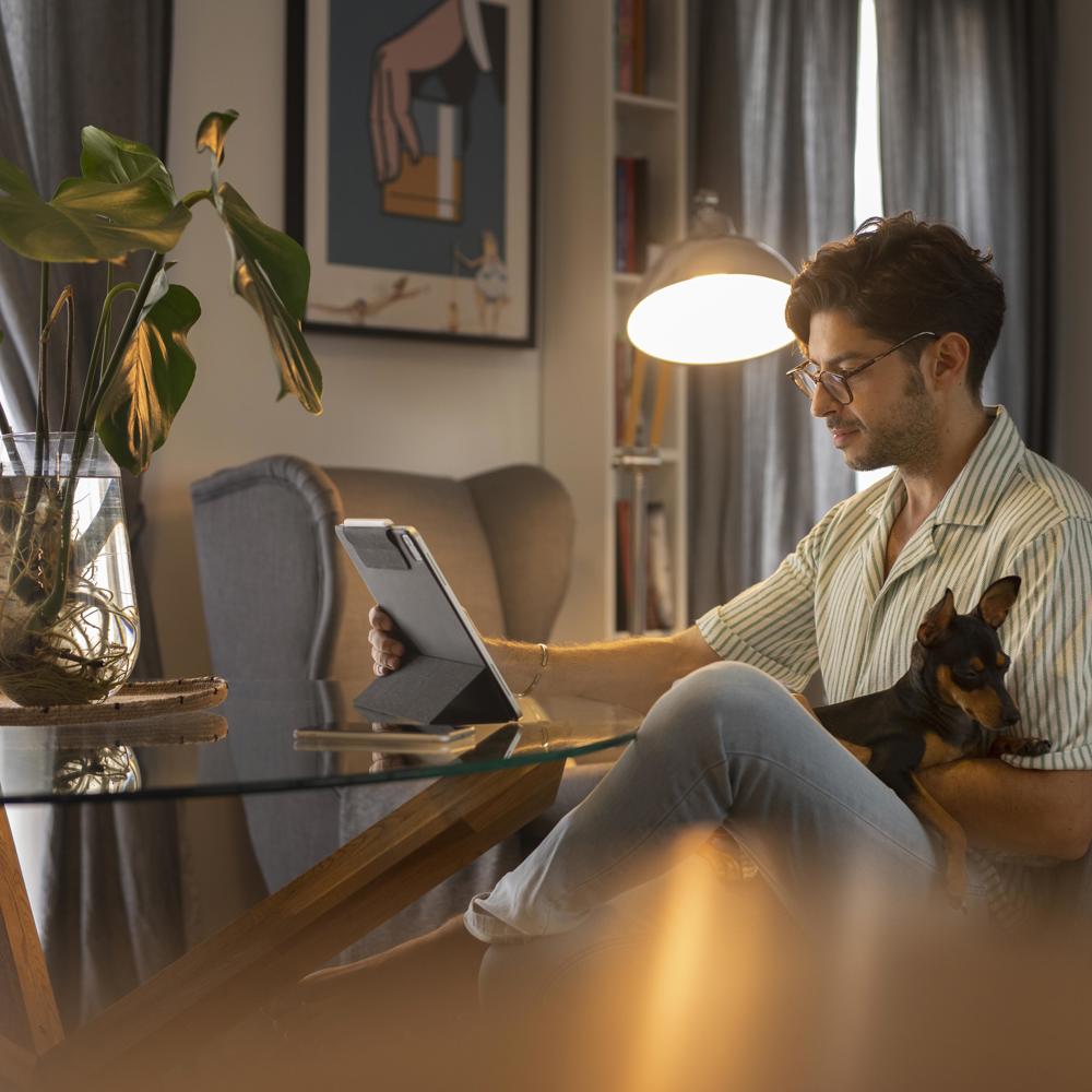 En man läser information på sin Ipad hemma med sin hund i knät. 