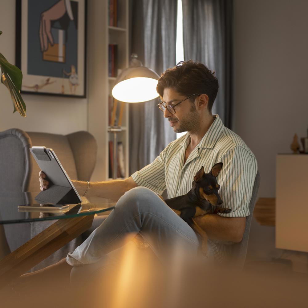 En man läser information på sin Ipad hemma med sin hund i knät. 